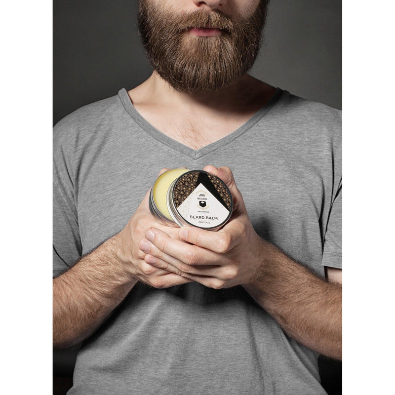 Bearded man in a gray shirt holding up a an open container of beard balm by Beard Reverence