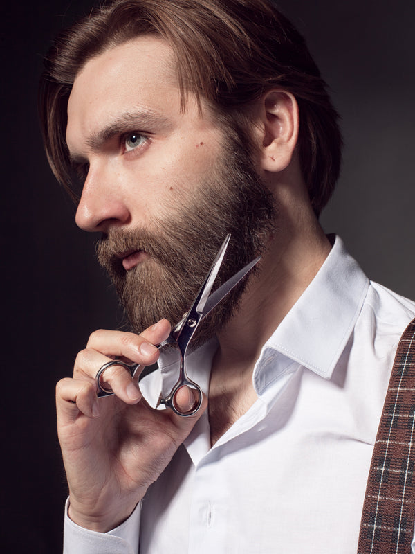 Dark haired bearded man using Beard Reverence scissors to trim his beard.  