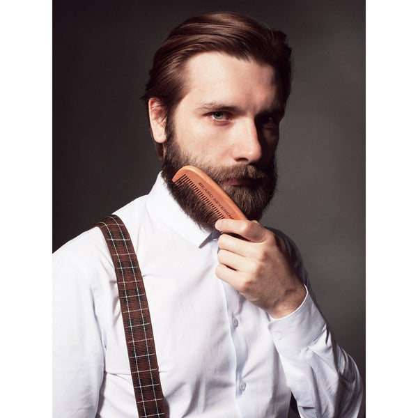 Man in overalls and white shirt combing through his beard with a wooden comb made by Beard Reverence