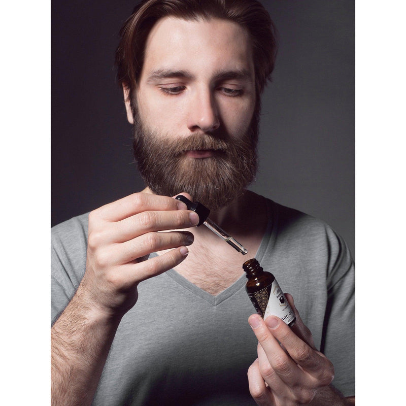 Dark haired bearded man demonstrating how to use a beard oil dropper